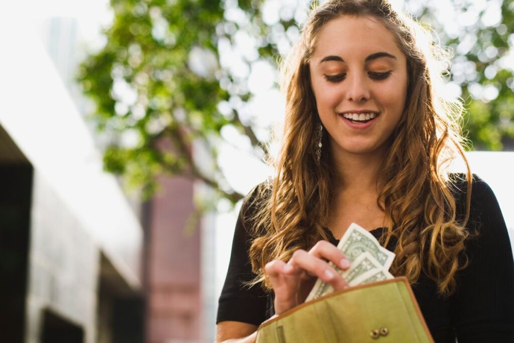 a girl standing on a sidewalk counting cash out of her wallet