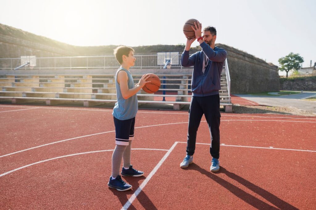 a teenage boy teaching a middle school boy how to play basketball