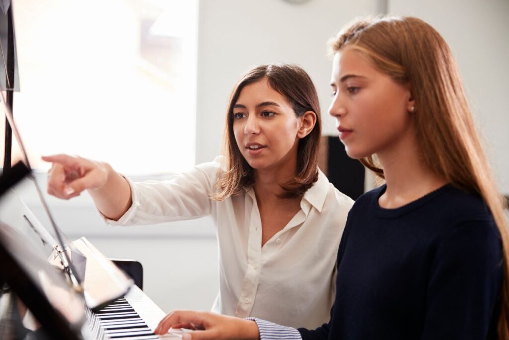 a teenage girl teaching a younger girl piano lessons