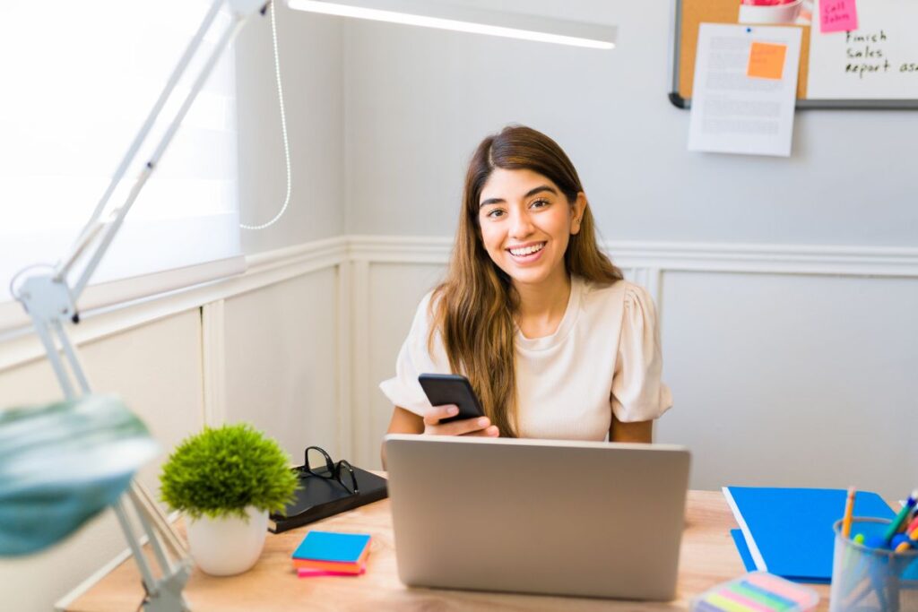 a teenage girl working on her phone in front of a computer in an office